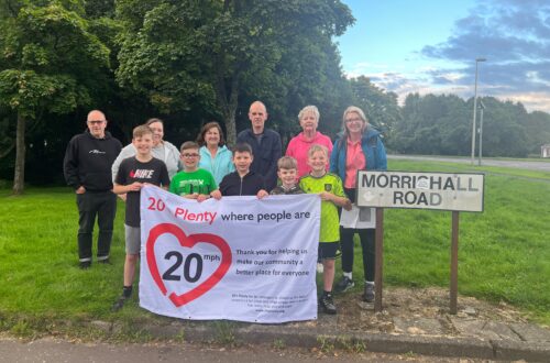 Group of residents standing next to the Morrishall Road street sign, holding a banner highlighting their support for a 20mph speed limit